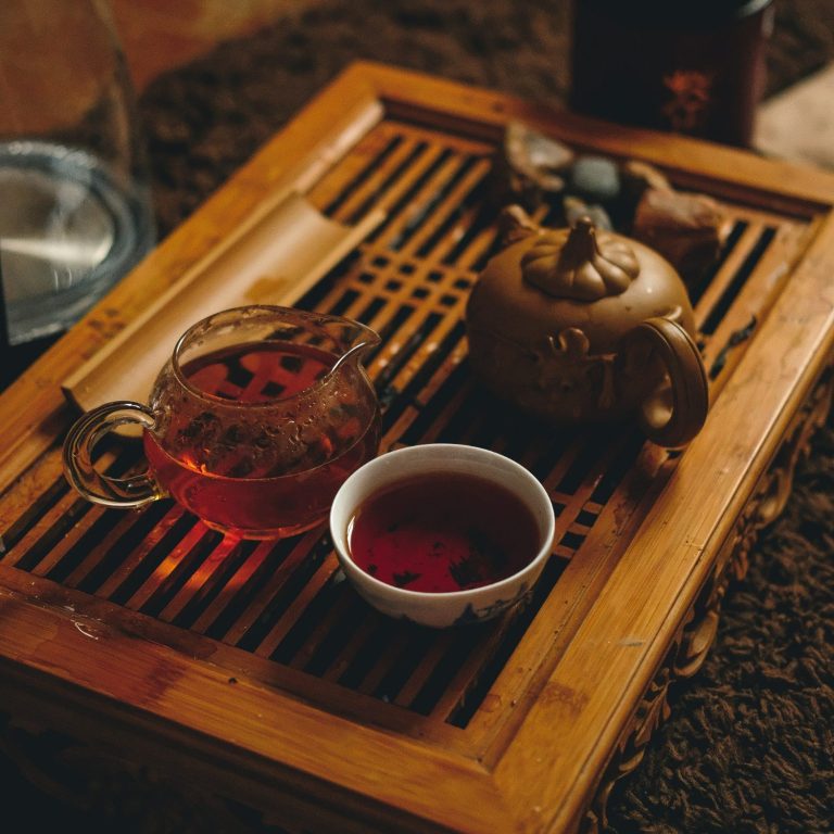 Un plateau en bois sur lequel est posé une théière en terre cuite, une théière en verre et un petit bol blanc avec du thé dedans.