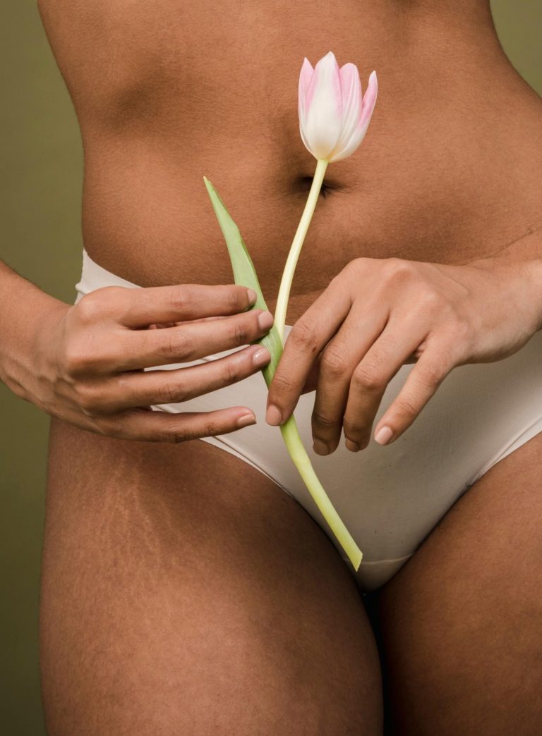 Une femme en culotte beige tient une tulipe avec ses mais devant son bas-ventre pour illustrer la guidance autour du cycle menstruel 